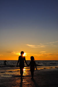 Silhouette people on beach against sky during sunset