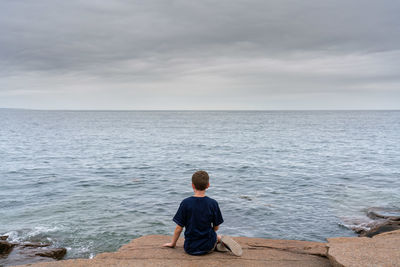 Rear view of man sitting at sea shore against sky