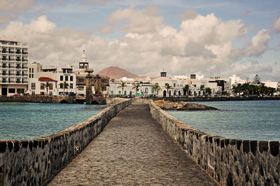 Walkway by sea against buildings in city