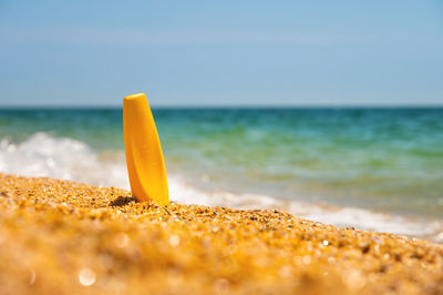 Sunscreen in the sand against the background of the sea. yellow tube of sun skin care product