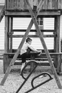 Full length of boy tying shoelace at built structure outdoors