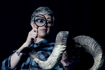 Close-up portrait of young woman holding eyeglasses against black background