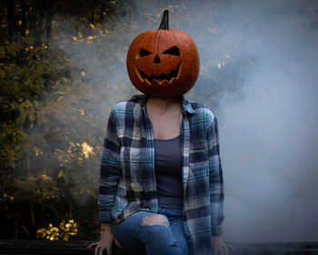 Young adult with a carved pumpkin head, fog, plaid, changing leaves,and ripped jeans