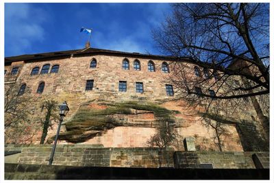 Low angle view of bare tree against built structure