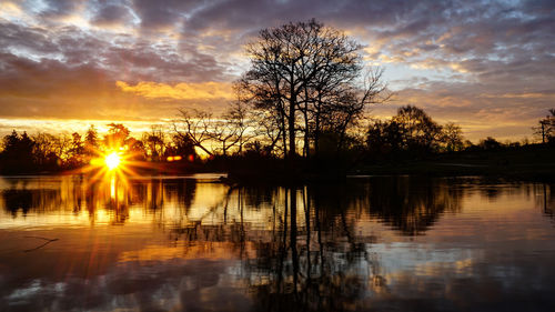 Silhouette trees by lake against sky during sunset