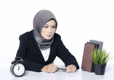 Portrait of young woman sitting on potted plant against white background