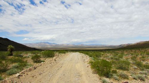 Dirt road amidst landscape against sky