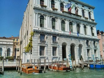 Boats moored in canal by buildings in city against clear sky