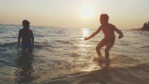 Full length of boys playing on beach against sky during sunset