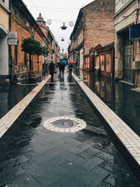 People carrying umbrella walking on wet street amidst buildings