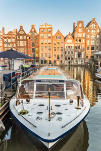 Boats moored on canal by buildings in city against sky