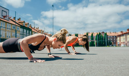 Women doing push-ups on land in city against sky