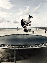 Boy jumping on trampoline at beach against sky