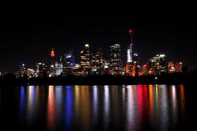 Illuminated buildings by river against sky at night