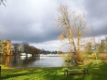 Bare trees by lake against cloudy sky