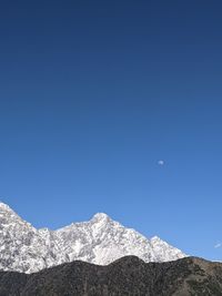 Low angle view of snowcapped mountains against clear blue sky