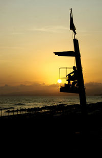 Silhouette bird on wooden post by sea against sky during sunset