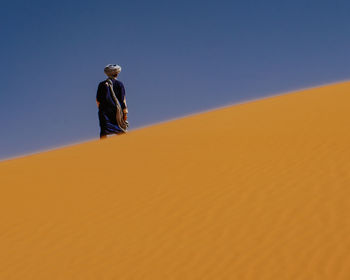 Man standing on sand dune in desert against clear sky