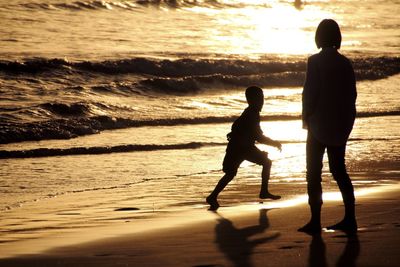 Silhouette boys standing at beach during sunset