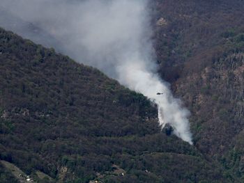 Helicopter dropping water on a forest fire above gordola, ticino, switzerland