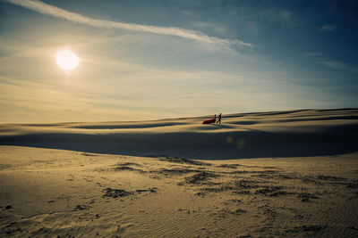 Couple on desert against sky during sunset