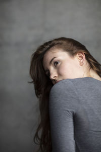 Beautiful young woman looking away against wall