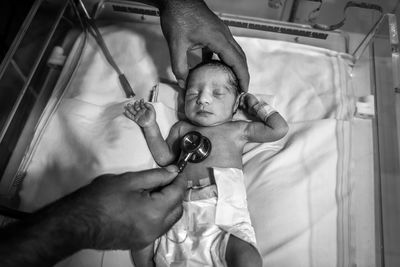 Cropped hands of male doctor examining baby boy on bed in hospital