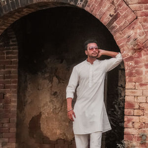 Portrait of young man standing against brick wall