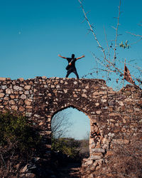 Man with arms outstretched standing against blue sky