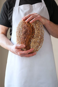 Close-up at bakers hands holding a loaf of organic sourdough bread in front of him.