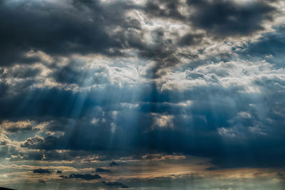 Low angle view of sunlight streaming through clouds