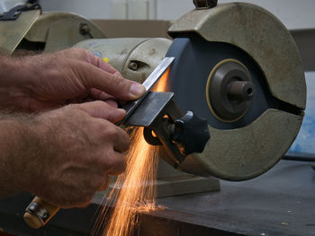 Cropped hands of man sharpening work tool on grinder 