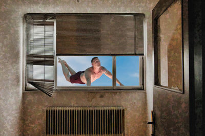 Shirtless man flying seen through glass window