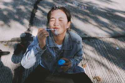 High angle view of beautiful woman blowing bubbles while sitting outdoors