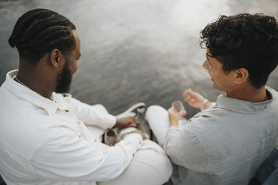 High angle view of young male friends enjoying while sitting near lake