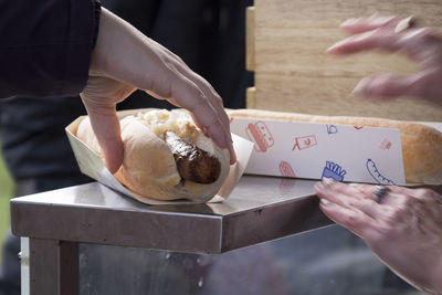 Cropped hand picking hot dog from table