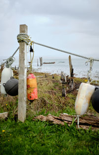 Close-up of wooden post on field by sea against sky