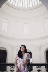 Portrait of young woman standing against railing