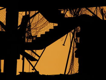 Silhouette cranes at construction site against sky during sunset