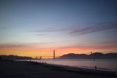 View of suspension bridge in calm sea at sunset