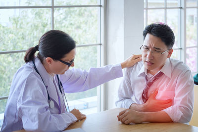 Close-up of female doctor examining patient at desk in hospital