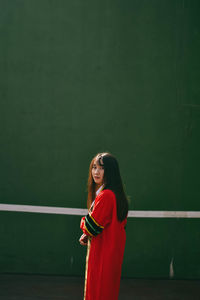 Portrait of young woman standing against wall