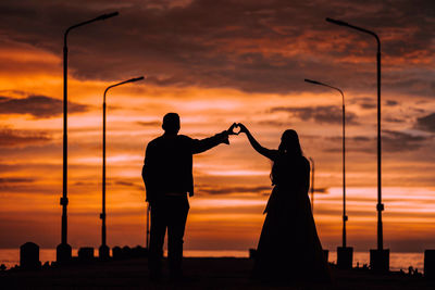 Silhouette friends standing against sky during sunset