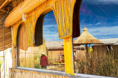 Man and thatched roof against house reflected on window