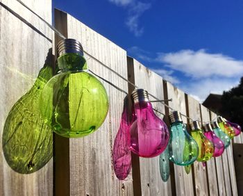 Low angle view of multi colored lightbulbs hanging against sky