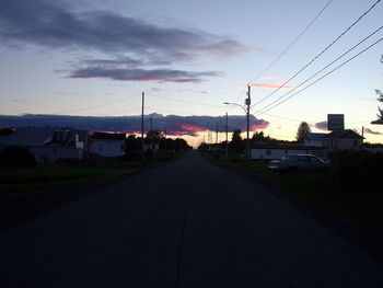 Road by houses against sky during sunset