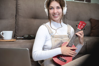 Beautiful young hipster girl in casual clothes learning to play the ukulele guitar while sitting on