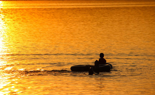 Silhouette man sitting in sea against sky during sunset