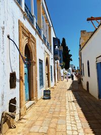 Footpath amidst buildings against blue sky