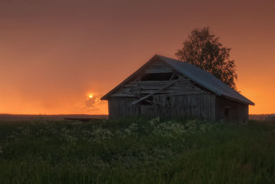 House on field against orange sky